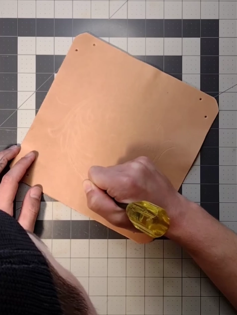 Leatherworker scribing a design onto tan leather at the workbench