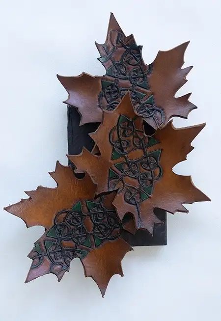 A set of three brown leather maple leaf wall decor pieces, each hand-tooled with Celtic knotwork displayed on a neutral surface..