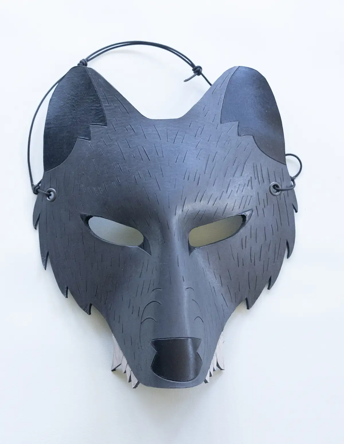 A gray leather wolf mask with a hand-embossed design and an adjustable black leather strap displayed against a neutral background.