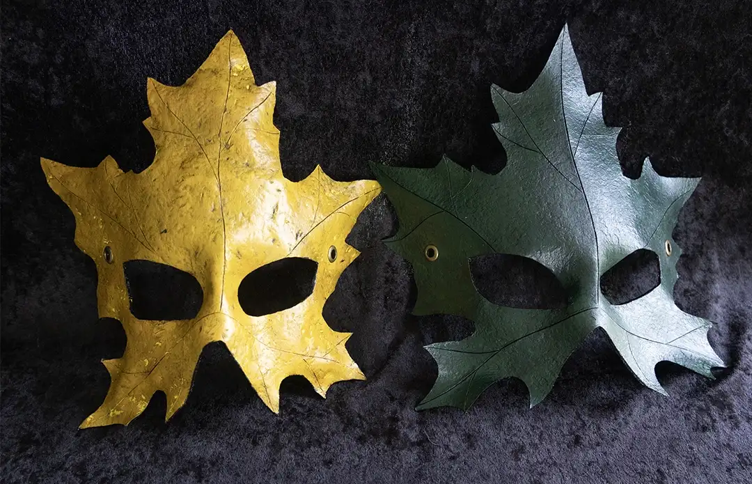 A green and a yellow leather maple leaf mask displayed side by side showing the available color options displayed against a dark background.