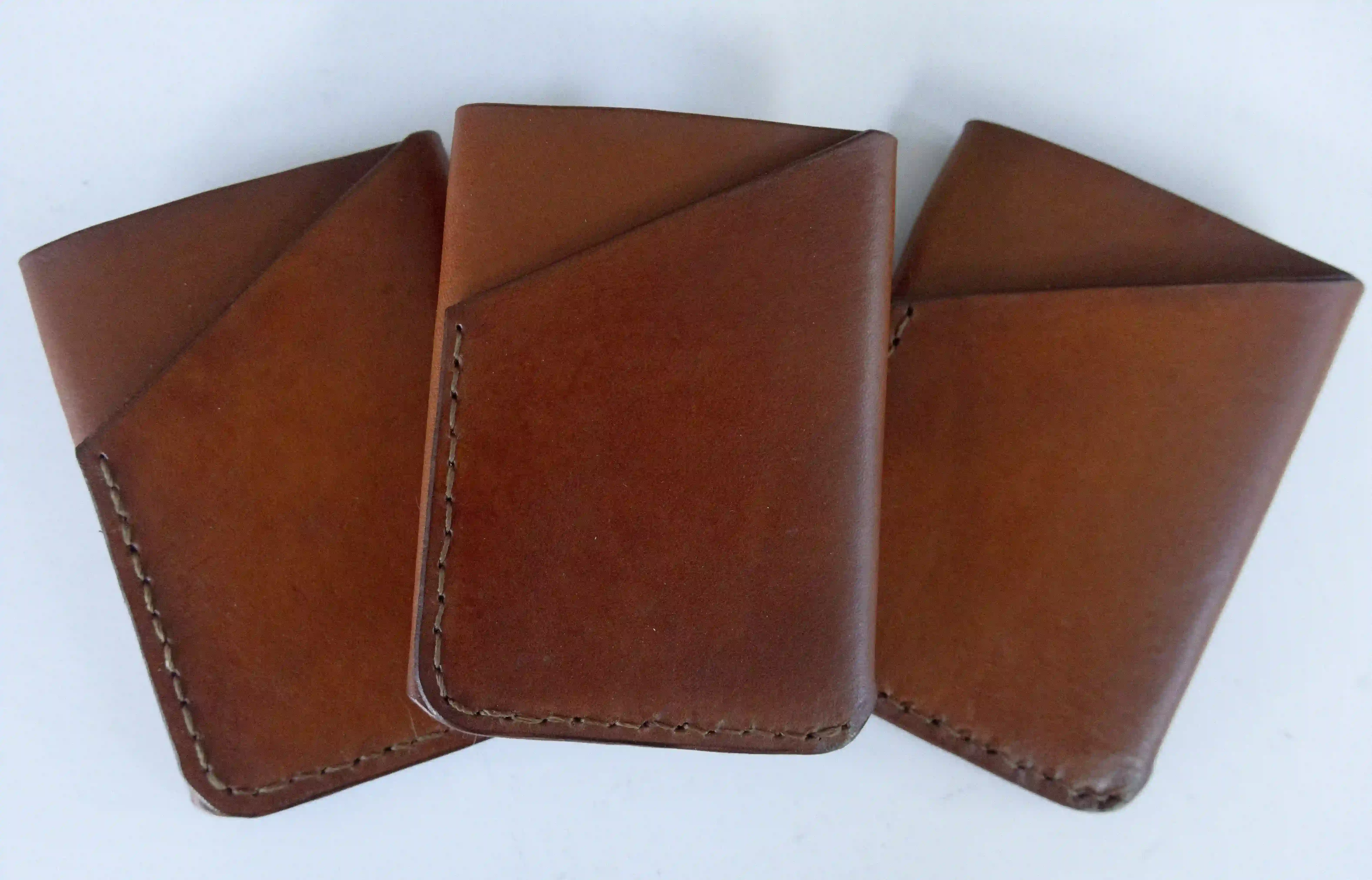 Three light brown leather three-pocket wallet displayed on a neutral surface.
